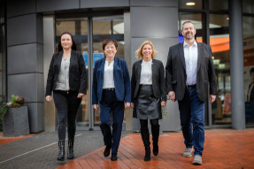 Berater und Beraterinnen der Firma ImmoKonzepte GmbH stehen vor einem grauen Gebäude und lächeln freundlich